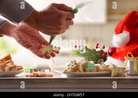 Dekorieren Sie Kekse mit weihnachtlichen Motiven mit farbiger Vereisung auf dem Küchentisch mit Utensilien. Draufsicht. Horizontale Zusammensetzung. Stockfoto