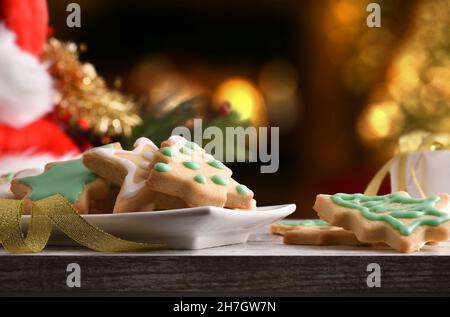 Holztisch mit Keksen mit frisch zubereiteten Weihnachtsformen auf Teller mit weihnachtlicher Dekoration auf weißem Hintergrund. Vorderansicht. Horizontal Stockfoto