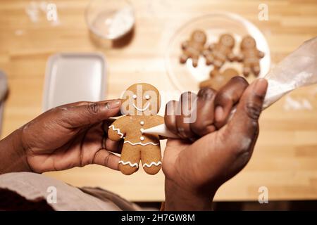 Hände junger afrikanischer Frauen, die weiße Glasur auf Lebkuchenkekse auftragen, während sie vor dem Urlaub festliche Speisen für die Gäste machen Stockfoto