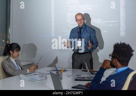 Selbstbewusster, reifer Coach oder IT-Ingenieur, der vor jungen interkulturellen Untergebenen oder Kollegen eine Präsentation macht Stockfoto