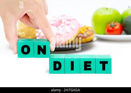 Text ZUR ERNÄHRUNG aus Buchstabenblöcken vor einem schwarzen Teller mit Süßigkeiten und einem weißen Teller mit Obst und Gemüse. Einen Plan für Veränderungen erstellen. Stockfoto