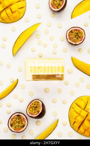 Draufsicht auf köstliche Mango- und Passionsfrucht-Mousse-Kuchenscheibe mit den angezeigten Schichten und Rezepturzutaten auf weißem Hintergrund. Restaurant-Menü und Süßwarenkonzept im Flat-Lay-Stil. Stockfoto