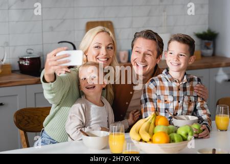 Glückliche Frau, die beim Frühstück mit der Familie Selfie auf dem Handy macht Stockfoto