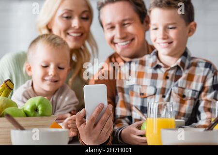 Mann, der Selfie auf dem Smartphone macht, fast unscharf glückliche Familie beim Frühstück Stockfoto