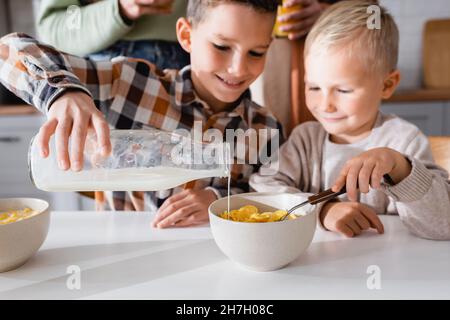 Kid Gießen Milch in Schüssel mit leckeren Cornflakes, während das Frühstück mit Bruder Stockfoto