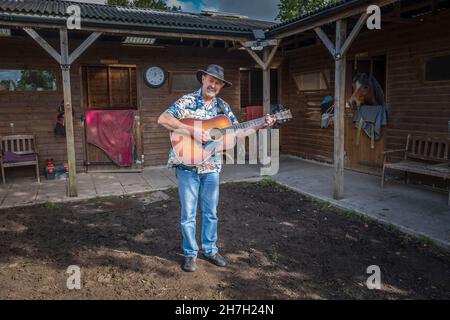Ein Mann, der vor den Ställen Gitarre spielt. Stockfoto