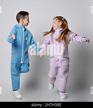 Verspielte, fröhliche Kinder, Junge und Mädchen in blauen und rosa Jumpsuits, laufen zusammen und schauen einander an Stockfoto