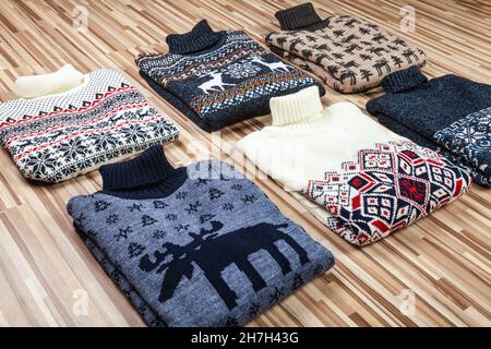 Verschiedene gestrickte weihnachtliche Rollkragenpullover mit nordischem geometrischen Ornament (Hässliche Pullover), gefaltet auf Holzhintergrund gelegt Stockfoto