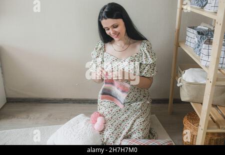 Eine junge Frau strickt zu Hause auf dem Boden einen warmen Schal. Stockfoto