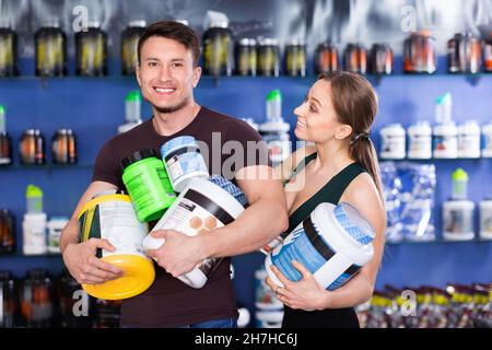 Glückliche junge sportliche Menschen stehen im Laden, halten große Dose Sportnahrung Stockfoto