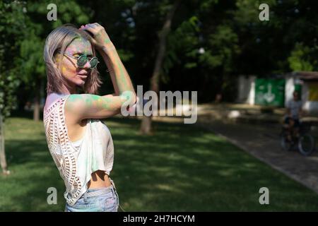 Mädchen auf dem Festival der Farben holi mit einem Gesicht in farbigen Puder. Glückliche Frau feiert indischen Urlaub im Park. Stockfoto