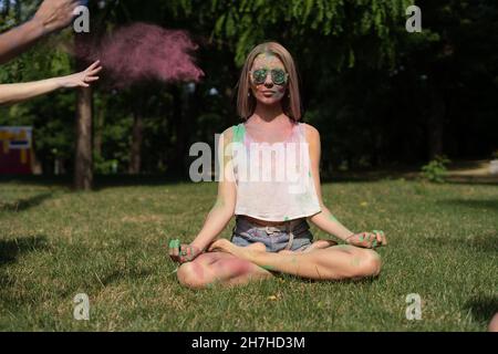 Junge Frau in der Lotusposition beim Holi-Festival meditiert in der Natur Pulverfarbe wird auf das Mädchen gegossen. Color Fest und Outdoor-Meditation. Stockfoto