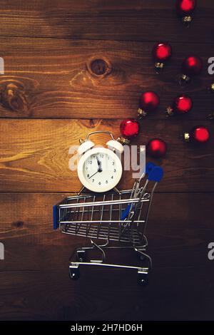 Wecker mit Mitternachtsanzeige, kleinem Wagen und bunten Weihnachtskugeln auf einem Holzhintergrund. Dunkler Weihnachtshintergrund. Stockfoto