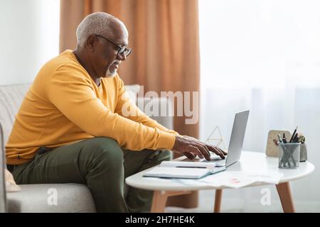 Seitenansicht Des Reifen Schwarzen Mannes Beim Tippen Auf Laptop Zu Hause Stockfoto