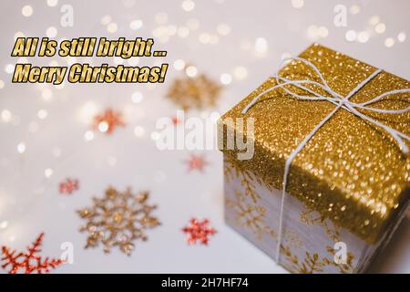 Alles ist noch hell ... Frohe Weihnachten, positive Botschaft in pandemischen Zeiten auf weißem Hintergrund mit Schneeflocken und glitzernden goldenen Weihnachtsgeschenk und Stockfoto