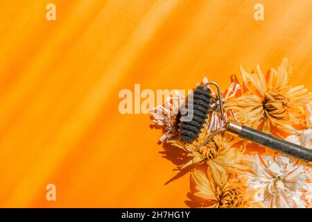 Ein Gesichtsmassager aus grüner Jade liegt zwischen trockenen Blumen auf einem gelben Hintergrund. Stockfoto