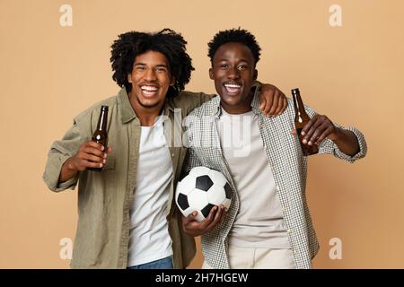 Fußballfans. Zwei Fröhliche Schwarze Halten Fußball Und Trinken Bier Stockfoto