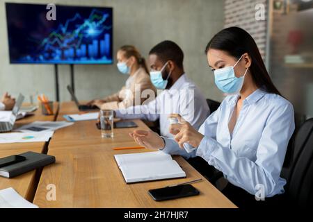 Neuer Normalwert. Asian Female In Face Mask Mit Desinfektionsmittel Spray Im Büro Stockfoto