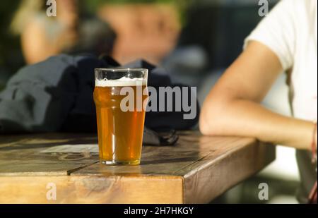 Junger Mann, der mit einem Glas Craft-Blondbier an einem Tisch sitzt, in der Außenbar mit Naturszene Stockfoto