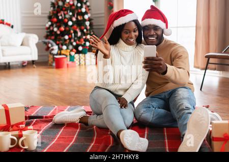 Schwarze Familie mit Handy macht Videocall auf Weihnachten winkende Hände Stockfoto