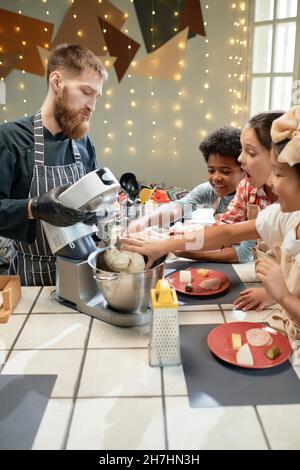 Gruppe von Kindern lernen, mit Hilfe des Kochs zu kochen, sie verwenden Mixer in ihrer Vorbereitung in der Küche Stockfoto