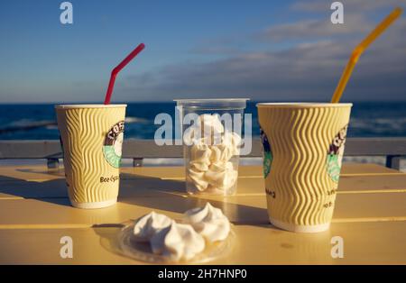 Zwei Pappbecher mit Kaffee und Marschmalchen auf einem Tisch mit Meereslandschaft im Hintergrund Stockfoto