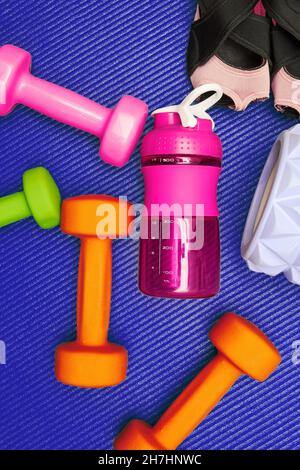 Vertikales Stillleben mit Fitnessgeräten, Hantel, Roller, Flasche auf der Matte. Gym Eqip und Gesundheitswesen Hintergründe Stockfoto