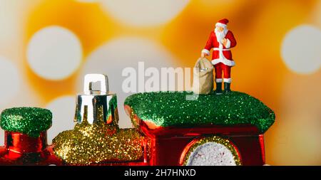 Ein Miniatur-weihnachtsmann mit einem Sack mit Geschenken auf einer Spielzeuglokomotive, auf einem Bokeh-Effekt-Hintergrund, in einem Panorama-Format als Webverbot zu verwenden Stockfoto