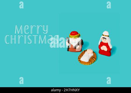 Die heilige Familie, gebildet vom Kind jesus, der Jungfrau maria und dem heiligen josef, und der Text fröhliche weihnachten auf blauem Hintergrund Stockfoto