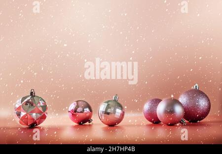 Rosa Weihnachtsbaumkugeln auf rosa Hintergrund mit fallendem Schnee Stockfoto