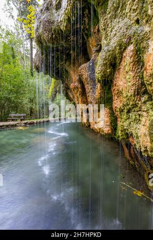 Kalkhaltiges kristallklares Wasser, das in eine Quelle fällt, Travertin-Quelle Kallektuffquell, Felsformation mit Moos, Bäumen und einer Bank im Hintergrund Stockfoto