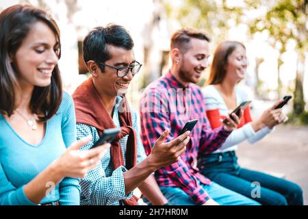 Multikulturelle Studenten lachen auf dem Universitätscampus mit dem Smartphone - Junge Leute Freunde, die vom Handy süchtig sind Stockfoto