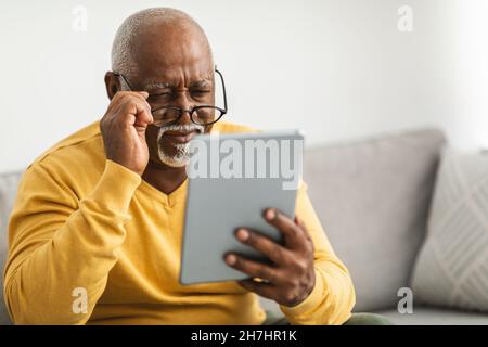 Älterer Mann Mit Schlechter Sehkraft, Der Die Augen Des Tablets In Der Halle Schielt Stockfoto