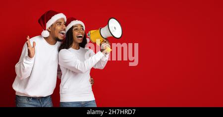 Emotionale schwarze Liebhaber in Weihnachtsmützen über Lautsprecher Stockfoto