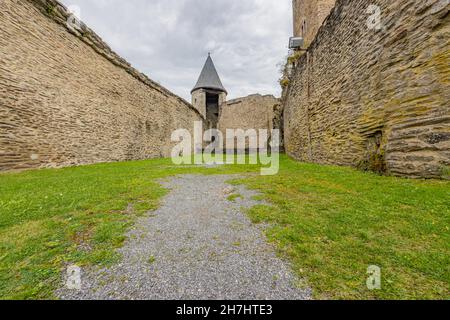 Grünes Gras auf dem Boden zwischen den verfallenen Steinmauern im Hintergrund der Wachturm, in der mittelalterlichen Burg von Bourscheid, bewölkten Tag mit Stockfoto