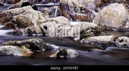 Abgerundete Granitfelsen im Bachbett mit Samt freiliegender Wasseroberfläche, die die Felsen umrundet Stockfoto
