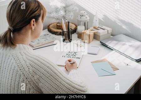 2022 Ziele, Neujahrsskende. Frau in weißem Pullover Schreiben Text Neujahrsauflösung in offenem Notizblock auf dem Tisch. Start ins neue Jahr, Planung und Stockfoto