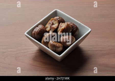 Quadratische Schüssel mit sechs gerösteten Kastanien auf einem Holztisch Stockfoto