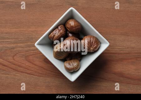 Quadratische Schüssel mit sechs gerösteten Kastanien auf einem Holztisch Stockfoto