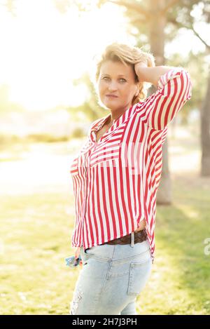 Porträt einer blonden kaukasischen Frau mittleren Alters, die auf die Kamera schaut und ihr Haar selbstbewusst berührt Stockfoto