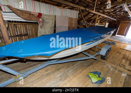 Kleine Glasfaser-Schiff auf Bootsanhänger, in Holzscheune gelagert Stockfoto