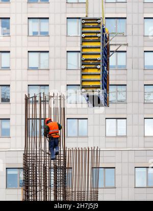 Ein Baumeister mit einer leuchtend orangefarbenen Weste und einem Schutzhelm installiert die Schalung auf einem Stahlrahmen für das anschließende Betongießen. Stockfoto