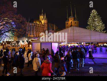 23. November 2021, Thüringen, Erfurt: Auf dem Erfurter Christkindlmarkt auf dem Domplatz unter dem Mariendom und der Severuskirche leuchten die Lichter. Die meisten thüringischen Städte wie Jena, Suhl und Nordhausen hingegen hatten aufgrund der besorgniserregenden Infektionszahlen ihre Weihnachtsmärkte abgesagt. Nun steht eine Verschärfung der Corona-Maßnahmen in den Angen. Am 24. November wird der landtag über weitere Einschränkungen diskutieren. Daher ist derzeit unklar, ob die Weihnachtsmärkte bis Ende Dezember geöffnet bleiben dürfen. Foto: Martin Schutt/dpa-Zentralbild/dpa Stockfoto