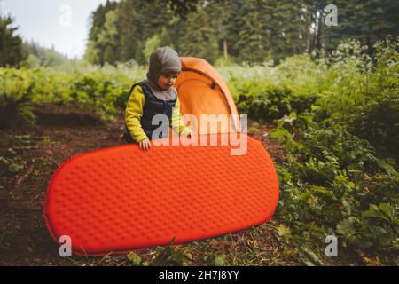 Kind mit Schlafpolster hilft, Camping Zelt Reise Familienurlaub Wandern im Freien in Wald Abenteuer Lifestyle Backpacking Reise gesetzt Stockfoto