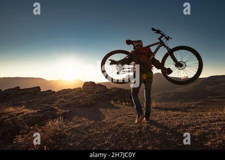 Sportlicher Radler klettert bei Sonnenuntergang mit dem Mountainbike bergauf Stockfoto