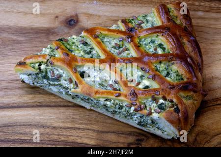 Pie mit Käse und Spinat auf einem Holzbrett. Eine Scheibe offener Spinatkuchen, bestreut mit Sesamsamen. Köstliche hausgemachte herzhafte Backwaren. Stockfoto