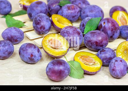 Frische rohe blaue und violette Pflaumen mit grünen Blättern auf hellem Holzgrund. Stockfoto