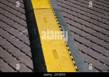 Kabelschlauchschutz auf Pflasterplatten. Sicherheitsabdeckung aus Gummi für den Kabelschutz bei Veranstaltungen im Freien. Ein Kabelschutzsystem schützt die elektrische Leitung Stockfoto