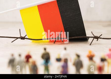 Stacheldraht, deutsche Flagge und Plastikspielzeugmänner außer Fokus, Konzept des illegalen Grenzübergangs durch Migranten Stockfoto