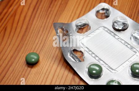 Eine Blisterpackung mit Medikamenten mit grünen Tabletten auf einem Holztisch Stockfoto